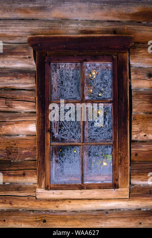 Arbre de Noël lumineux à peine visible derrière la fenêtre avec verres gelés dans le journal d'un vieux mur de construction en bois Banque D'Images
