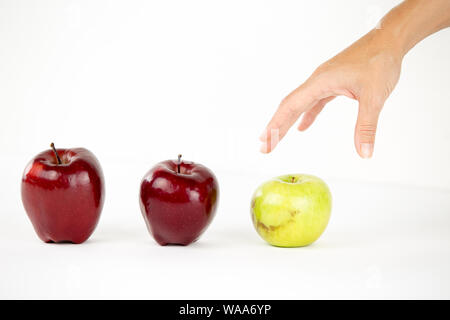 Concept de diversité : a woman's hand est sur le point de saisir la seule pomme verte parmi les autres rouges Banque D'Images