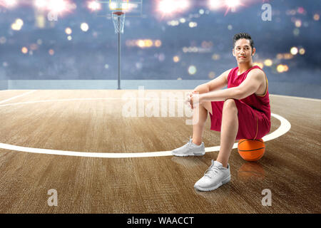 Joueur de basket-ball homme asiatique assis sur la balle sur le terrain de basket-ball Banque D'Images