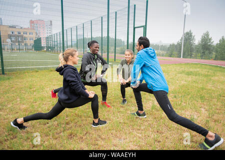 Groupe de jeunes gens sympathiques multiculturelle doing stretching exercice pour les jambes Banque D'Images
