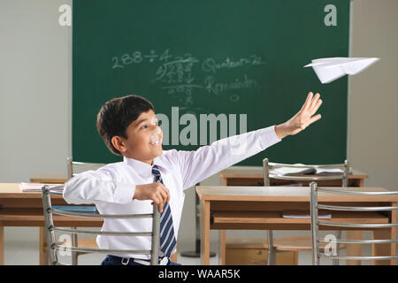 Un écolier jouant avec un avion en papier dans une salle de classe Banque D'Images