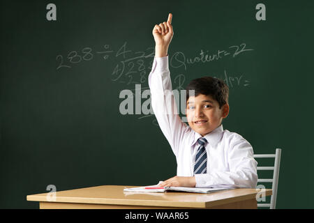 Schoolboy raising hand in classroom Banque D'Images