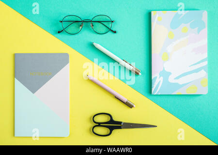 Deux des cahiers, stylos, ciseaux et lunettes sur fond jaune et bleu Banque D'Images