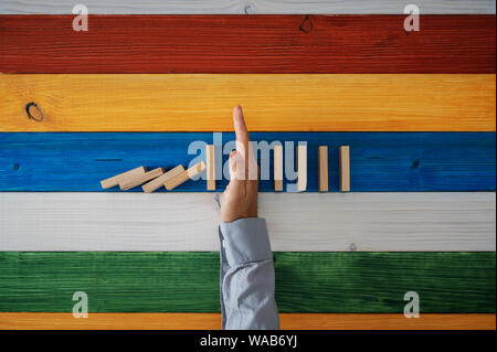 Vue du dessus de la main de l'homme d'arrêter la chute de dominos sur fond coloré de planches en bois. Banque D'Images