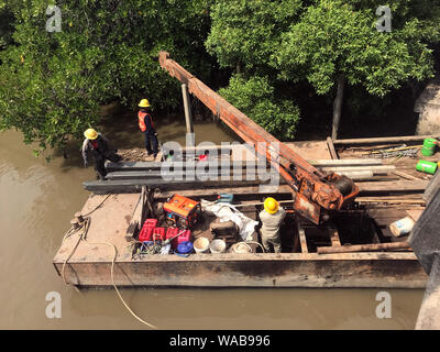 Équipe de travailleurs tirez des colonnes de béton hors de l'eau sur le fer avec ponton grue. La reconstruction de la côte du fleuve, Thaïlande Banque D'Images