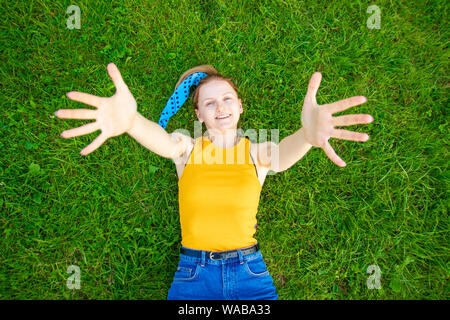 Grand moments d'été. Cheerful blonde woman stretching out arms se trouve sur l'herbe verte Banque D'Images