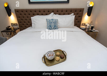 Cappuccino avec du chocolat sur le dessus de la conception de fantaisie avec trhee divers biscuits cuits sur le plateau d'or dans chambre d'hôtel sur bed Banque D'Images