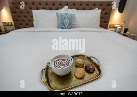 Cappuccino avec du chocolat sur le dessus de la conception de fantaisie avec trhee divers biscuits cuits sur le plateau d'or dans chambre d'hôtel sur bed Banque D'Images