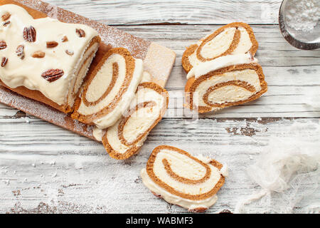 Belle fresh baked pumpkin spice cake rouleau avec du sucre en poudre, pacanes, garniture de fromage à la crème et blanc givre sur fond de table rustique. Vue d'en haut Banque D'Images