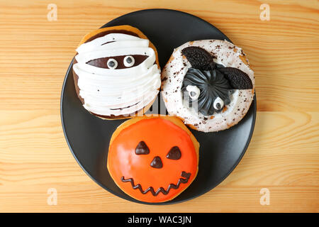 Vue du haut de trois différents types d'Halloween Donuts sur la plaque noire servi sur table en bois Banque D'Images