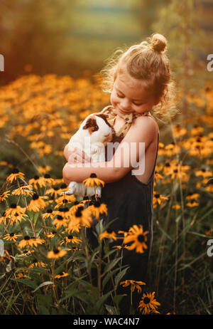 Petite fille se blottissant son animal de cobaye dans un champ de fleurs Banque D'Images