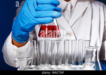 Dans un laboratoire de chimie, un homme est un pharmacien de l'analyse d'une fiole avec un liquide rouge. Expérience médicale avec un tube. Chimiste travaillant sur un essai gant bleu Banque D'Images