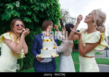 Les nouveaux mariés et les demoiselles d'avoir du plaisir et manger le gâteau ensemble dans l'air frais sur le banquet de mariage. Banque D'Images