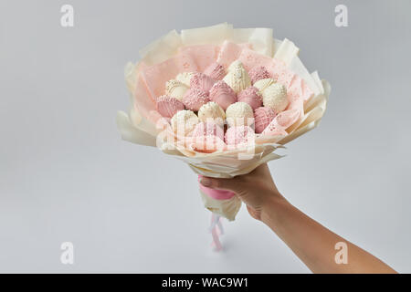 Beau bouquet d'offres composé de fraise mûre, recouvert de chocolat blanc et rose dans une main de femme Banque D'Images