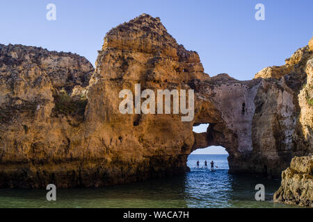 Trois pensionnaires de la palette sous une arche de roche rougeâtre sur leur chemin à partir de la mer ouverte à une baie. Soleil du matin rend la scène colorée. Ciel bleu et l'eau de mer Banque D'Images