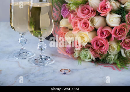 Un beau bouquet de roses délicates, une bague avec un diamant, deux verres de champagne sur une table en marbre. Jour de fête, un mariage. Valentine's Day Banque D'Images