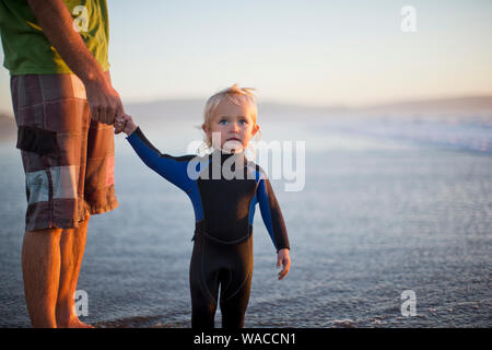 Jeune enfant en tenant la main de son père tout en vous tenant à côté d'un lac de porter une combinaison isothermique. Banque D'Images