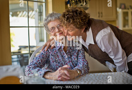 Smiling mature woman la salue cheerful mère âgée comme elle s'assoit à la table de la cuisine. Banque D'Images