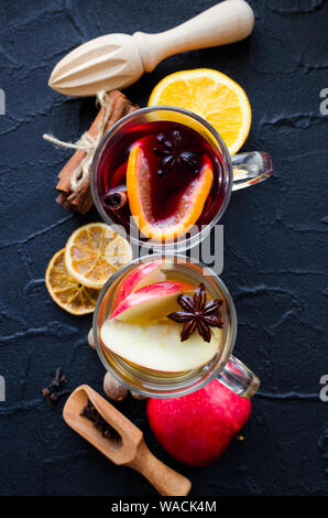 Deux verres de différents type de vin chaud ou de gluhwein basé sur les vins rouge et blanc avec des épices et ingrédients sur fond noir. Chaud épicé bever Banque D'Images