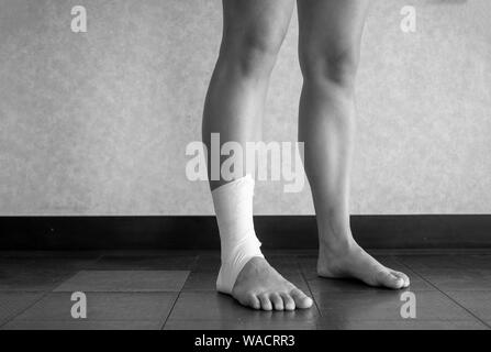 Version noir et blanc de l'athlète debout avec une cheville travail sur bande sur leur cheville blessée Banque D'Images