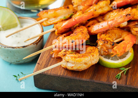 Brochettes de crevettes grillées ou langoustines servies avec de la chaux, de l'ail et de la sauce sur fond de béton bleu clair. Fruits de mer Banque D'Images