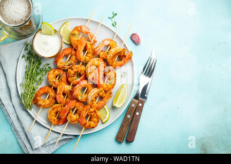 Brochettes de crevettes grillées ou langoustines servies avec de la chaux, de l'ail et de la sauce sur fond de béton bleu clair. Fruits de mer et bière. Vue de dessus avec copie Banque D'Images