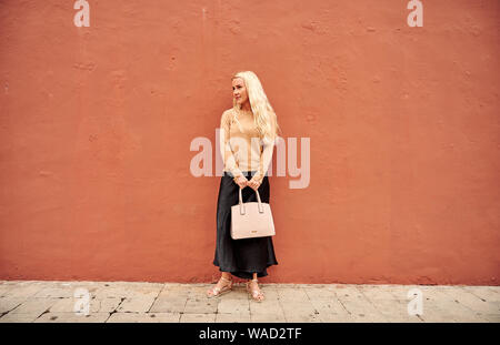 Très jolie jeune femme aux cheveux longs s'appuyant sur le mur d'orange et la tenue de sac dans la rue ville de Tenerife Banque D'Images