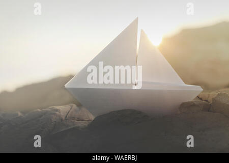 le bateau origami navigue sur les rochers illuminés par le coucher du soleil Banque D'Images