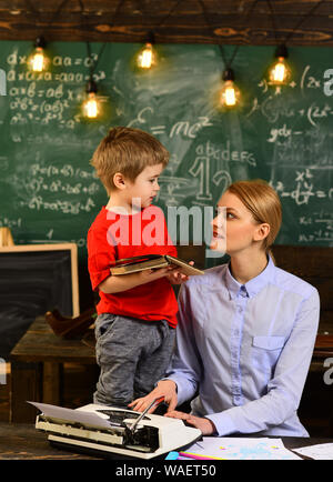 L'enseignant moderne écrit hipster sur grand tableau noir avec formule math Tutor, assise à côté de bureau au cours des leçons privées à la maison, l'homme à la recherche d'ordinateur portable Banque D'Images