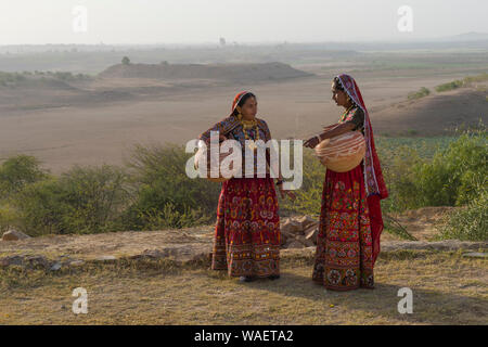 Deux femmes Ahir en tissu coloré traditionnel portant de l'eau dans une cruche d'argile, Grand Désert du Rann de Kutch, Gujarat, Inde Banque D'Images