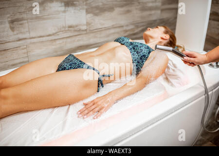 Belle femme en maillot de bain allongée sur le lit humide sous la douche chaude, ayant un hydromassage dans le spa salon Banque D'Images