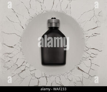 Un parfum noir, parfum ou parfum bouteille, avec copie espace, qui semble avoir atterri sur terre à partir d'un autre monde comme c'est créé un cratère. Banque D'Images