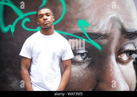 Un jeune homme pose devant un mur de graffiti art portrait sur une rue de ville n London Banque D'Images