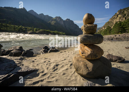 Pyramide en pierre équilibrée sur une plage avec une rivière et des montagnes en arrière-plan. Banque D'Images