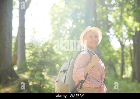 Portrait of senior woman in casual hat et avec sac à dos derrière son dos smiling at camera while standing outdoors in sunny summer day Banque D'Images