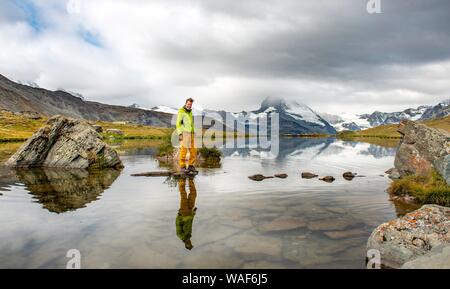 Randonneur marche sur des pierres dans l'eau, lac Stellisee, nuageux Matterhorn, Valais, Suisse Banque D'Images