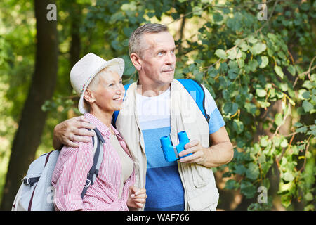 Happy senior couple de randonneurs enlacés et à la recherche à vue tout en debout dans la forêt et profiter de la nature ensemble Banque D'Images