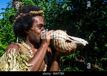 L'homme qui souffle dans une coquille géante, Ekasup village culturel, Efate, Vanuatu Banque D'Images
