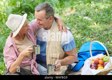 Mature Woman sitting et embrassant son homme pendant qu'ils boire le thé chaud pendant leur pique-nique dans la nature Banque D'Images