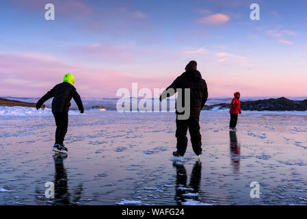 La Russie, Sarma - 3 janvier, 2019 : Trois personnes patiner sur la glace du lac Baikal et avoir un amusement à la lumière jaune orange coucher du soleil de soirée d'hiver. Bénéficiant d Banque D'Images