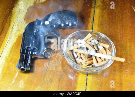 Pistolet revolver et cigarette dans le cendrier en verre table en bois Banque D'Images