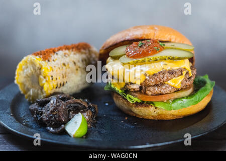 Burger All-American. Une chambre double et de graisse wagyu mélange chuck patty et bacon ketchup dans un pain brioché. Servi avec du maïs mexicain et thym sautés mushroo Banque D'Images