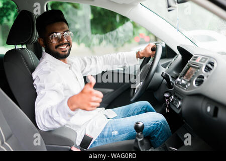 Young Asian man smiling and showing thumb up dans sa voiture. Banque D'Images