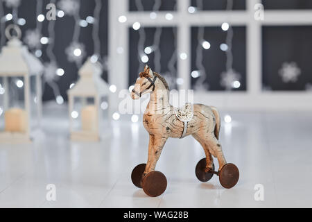 Jouet cheval de bois sur roues sur l'arrière-plan des lumières garland sur un plancher en bois blanc Banque D'Images