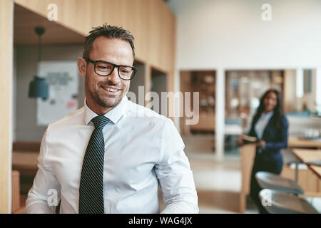 Mature businessman smiling while walking in a modern office avec un collègue debout dans l'arrière-plan Banque D'Images