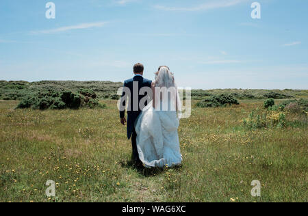 Mariée et le marié marcher à travers un champ de vert le jour de leur mariage Banque D'Images