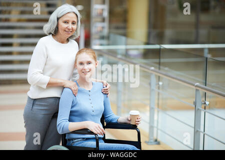 La haute mère embrassant sa fille handicapée en fauteuil roulant et ils smiling at camera dans le centre commercial moderne Banque D'Images