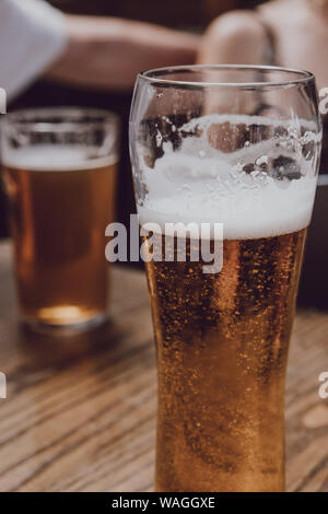 Gros plan d'une bière sur une table en bois, des personnes non identifiées sur le background, selective focus. Banque D'Images