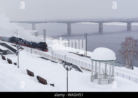 Paysage de neige d'hiver avec locomotive à vapeur se déplaçant le long de la rivière avec une rotonde et pont vintage automobile dans l'arrière-plan Banque D'Images