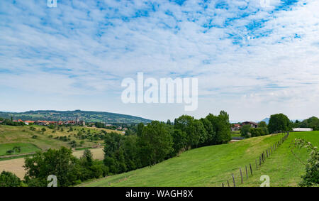 Vallonné et pittoresque paysage de prairies, de pâturages, champs, arbres, ville de Brens et les nuages blancs dans le ciel bleu. Banque D'Images